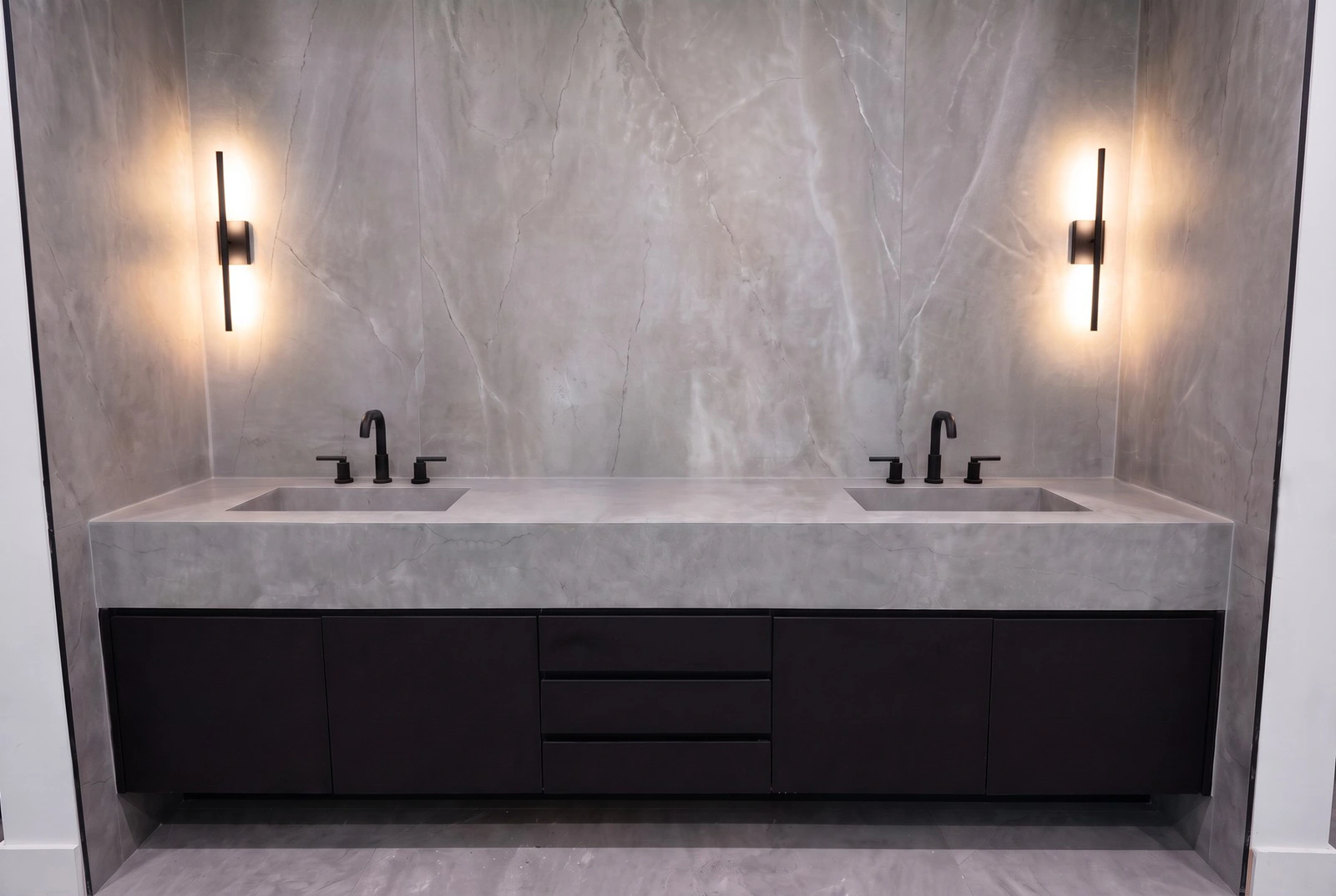 Double vanity with integrated stone sinks, full-slab stone walls and black wall sconces