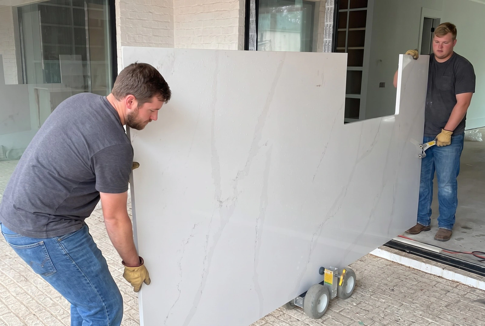 Two installers carrying a white quartz countertop on a slab cart into a home
