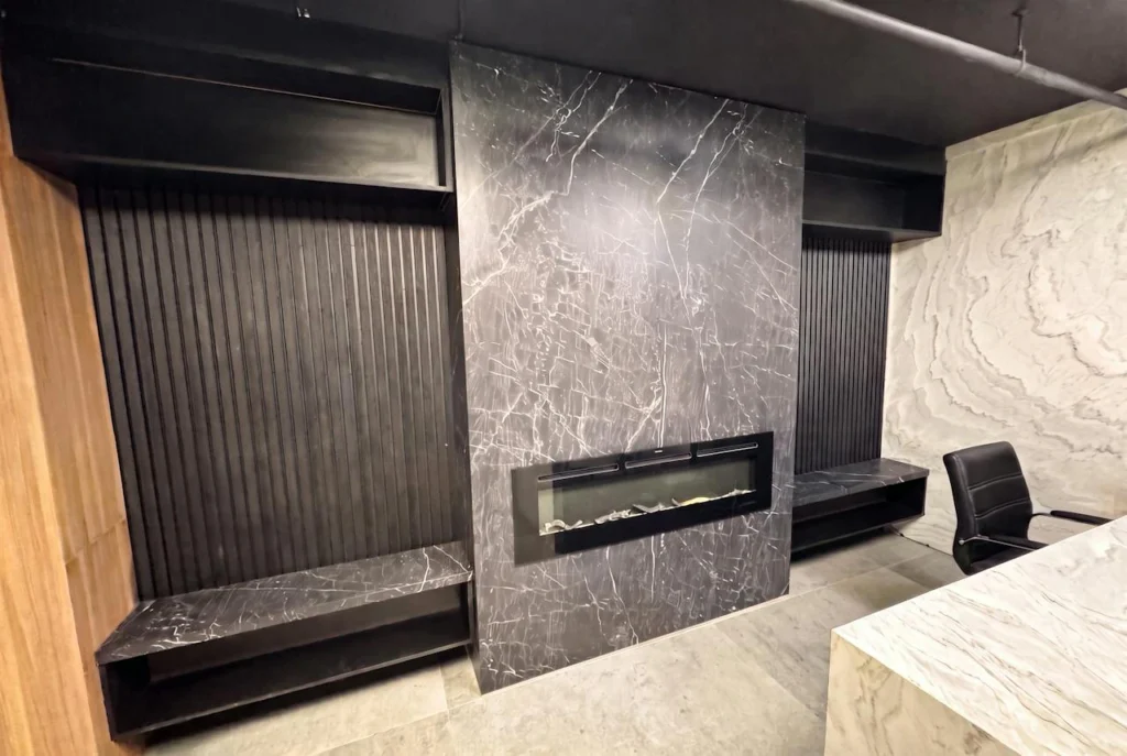 Floor-to-ceiling dark marble-look stone fireplace wall with matching floating benches between black fluted panels, fabricated by GA Granite